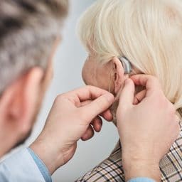 Audiologist inserting hearing aid on a senior woman's ear, close-up.