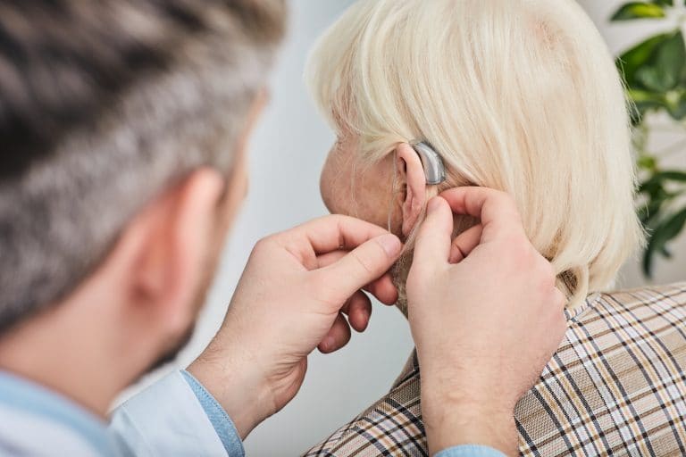 Audiologist inserting hearing aid on a senior woman's ear, close-up.