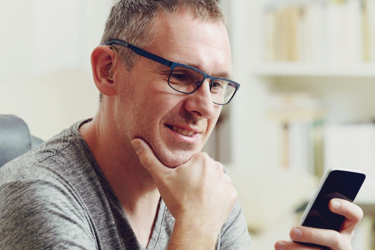 Hearing impaired man with hearing aid using smart phone at home or at office