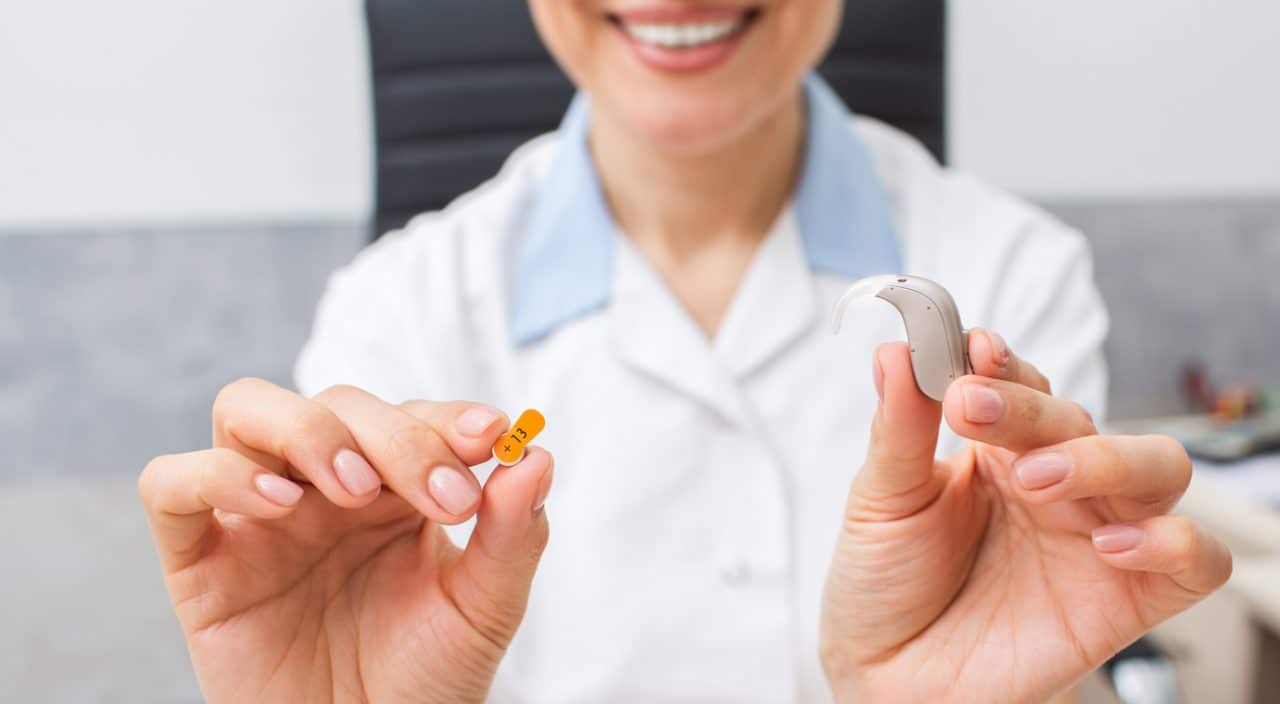 Audiologist holding a hearing aid and battery.