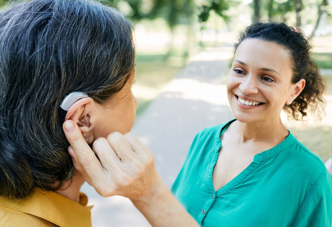 Woman with a hearing aid talking with her friend outdoors.